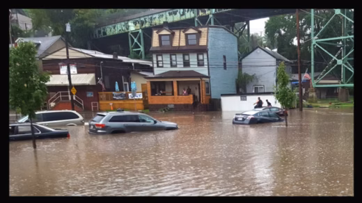 A Four Mile Run resident and his 8-year-old son trapped on top of their car await rescue during the 2016 flood. The stormwater project meant to prevent floods like this was defunded in late 2024. Photo by Justin Macey